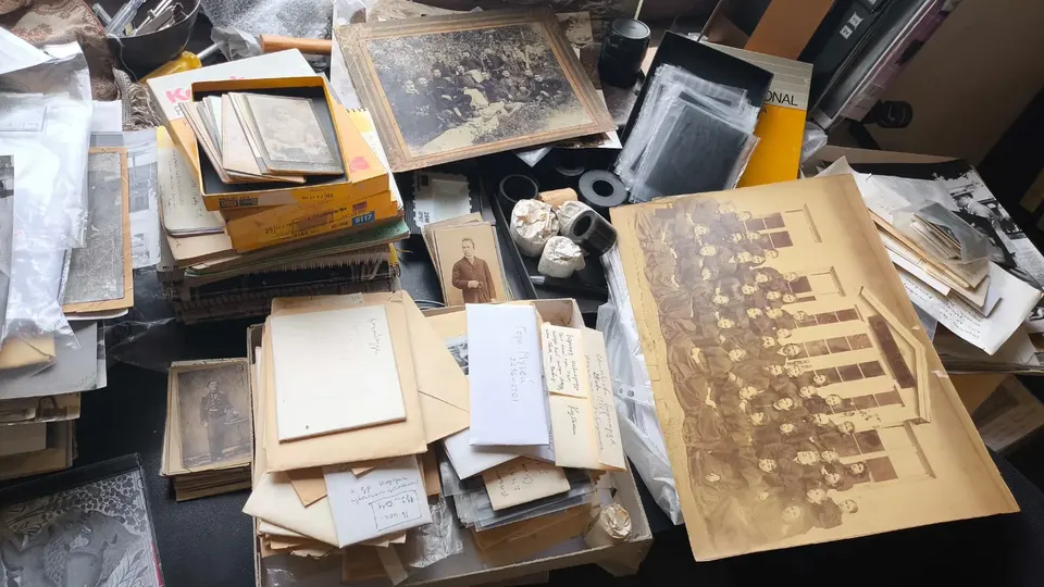 A museum archive desk covered in photographs, negatives, Kodak print boxes and handwritten record labels.