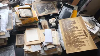 A museum archive desk covered in photographs, negatives, Kodak print boxes and handwritten record labels.